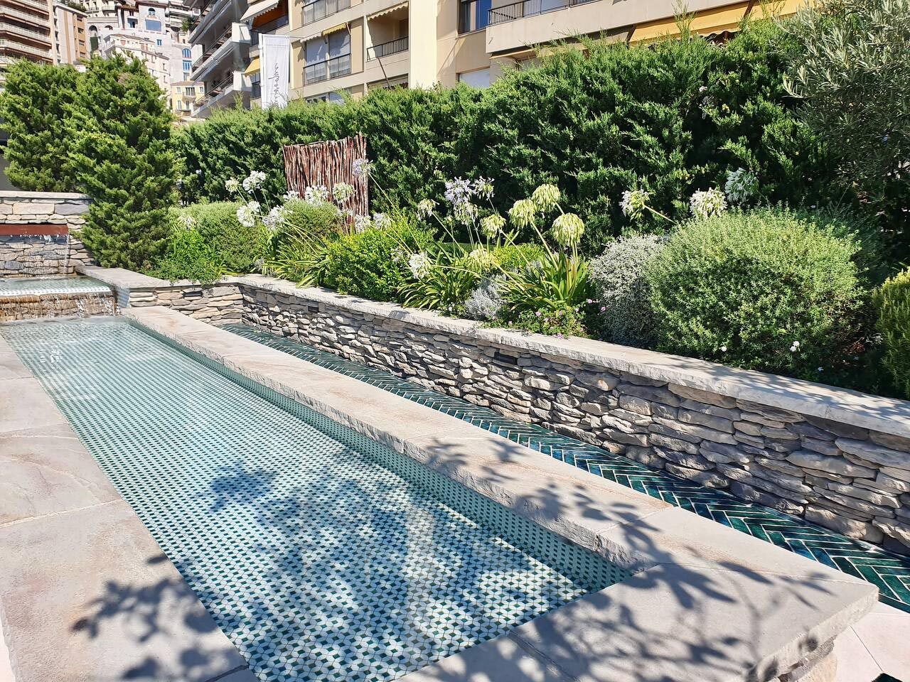 Vasca d'acqua lineare rivestita in mosaico verde, delimitata da un muro in pietra a secco, Monaco